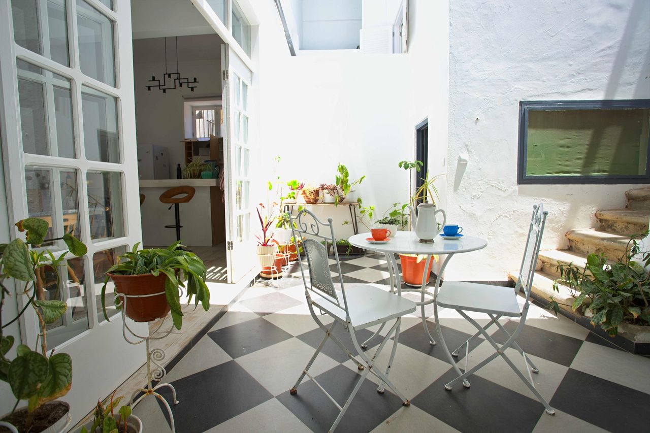 Pátio interior com mesa de café, plantas e chão axadrezado a preto e branco