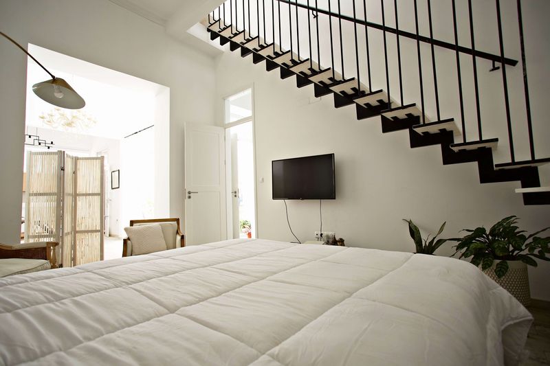 Cama de casal numa divisão com escada de madeira e ferro, televisão e candeeiro de pé