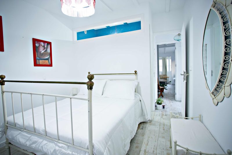 Quarto branco com cama de ferro, candeeiro vermelho e quadros coloridos