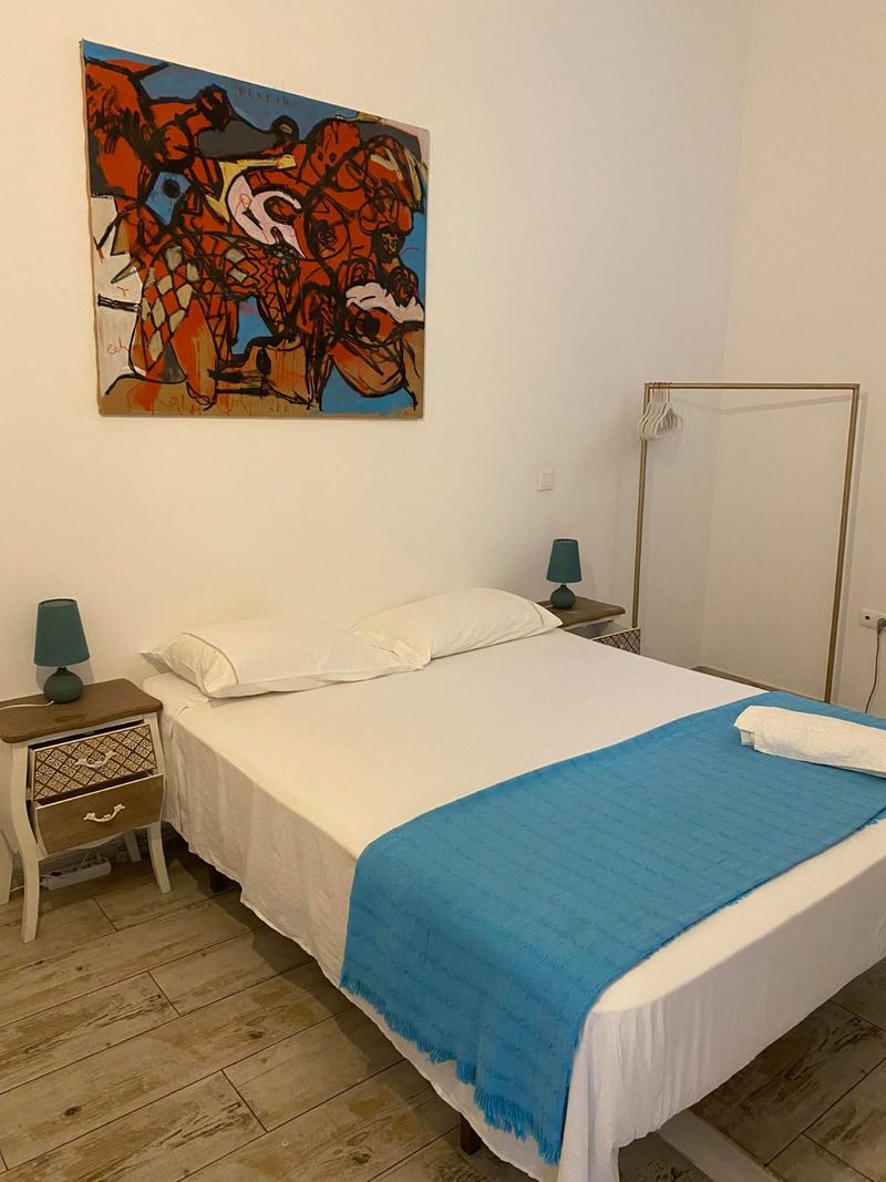 Quarto com cama de casal, manta azul e quadro de cores vivas na parede