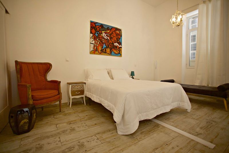 Quarto com poltrona laranja, mesa de cabeceira e pintura na parede