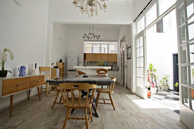 Sala com mesa de refeições e cozinha ao fundo, junto às portas de vidro do pátio